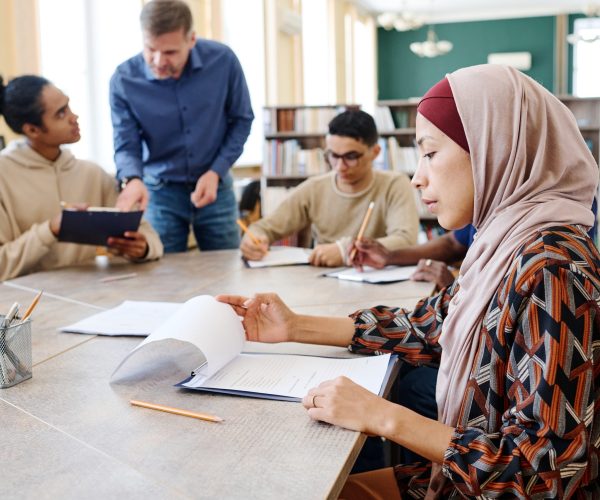 Muslim Woman During Class Muslim female immigrant sitting at table looking through sheets of paper with grammar tasks during English lesson
